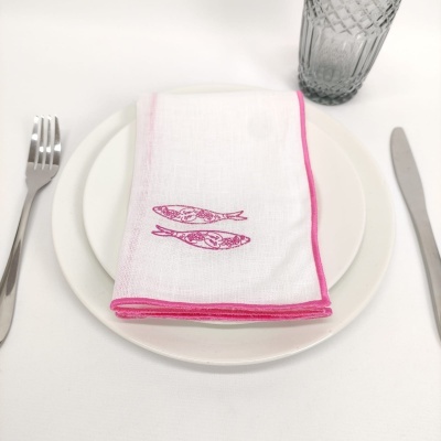Conjunto de pratos brancos com guardanapo com desenho de peixes rosa e talheres e copo ao lado