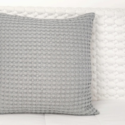 Almofada cinza texturizada sobre manta branca tricotada