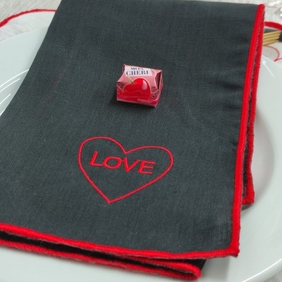 Guardanapo preto com bordado LOVE e bombom vermelho em prato branco
