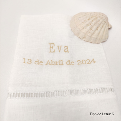 Toalha branca bordada com nome Eva e data 13 de Abril de 2024 ao lado de uma concha