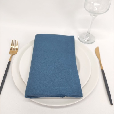 Conjunto de jantar com pratos brancos, guardanapo azul, talheres dourados e pretos e copo de vidro transparente