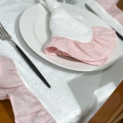 Toalha de mesa branca com borda rosa e guardanapo em prato branco numa mesa de madeira