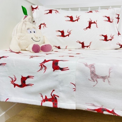 Lençol e almofada brancos com renas vermelhas e peluche de alho na cama branca