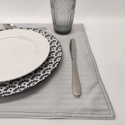 Conjunto de jantar com pratos, faca, guardanapo cinzento e copo de vidro cinzento.