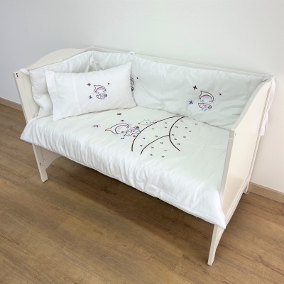 Berço branco com roupa de cama branca decorada com desenhos cor-de-rosa, lilás e preto