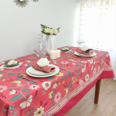 Mesa de madeira com toalha de mesa rosa com flores, pratos brancos, guardanapos rosa, flores brancas e velas acesas