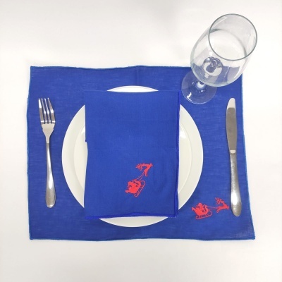 jogo americano azul com guardanapo azul com bordado vermelho, prato branco, talheres metálicos e copo de vidro