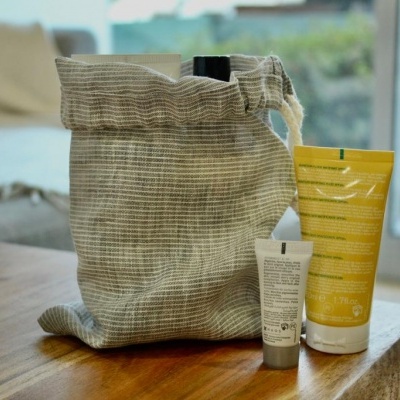 Saco de tecido cinzento com dois tubos de creme amarelo e branco sobre madeira numa sala