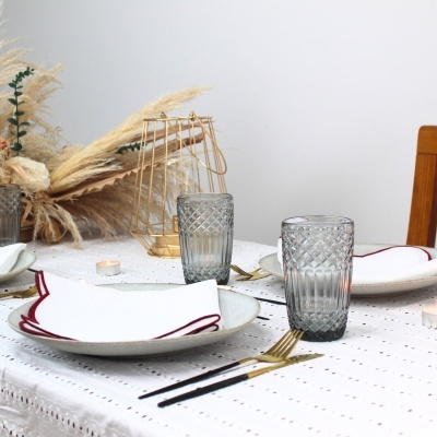 Mesa posta com pratos brancos, copos cinza texturizados e decoração com plantas secas.