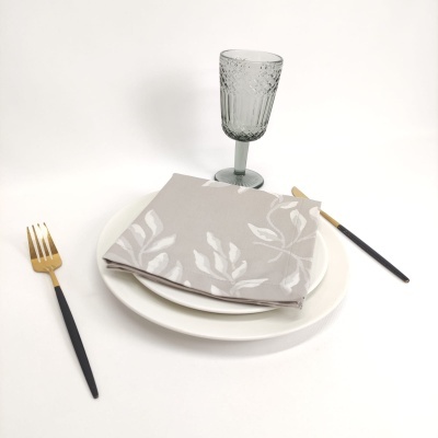 Mesa posta com prato branco, guardanapo estampado, talheres pretos e dourados e copo cinzento