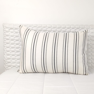 Almofada branca com riscas pretas sobre cama branca com cabeceira texturizada