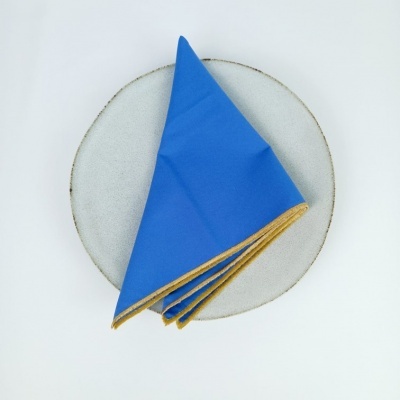 Guardanapo azul com bordo dourado sobre prato branco com bordo cinza