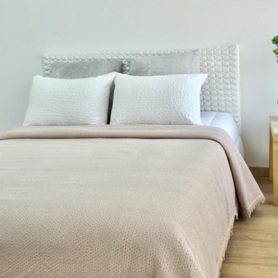 Cama de casal com cabeceira branca, cobertor bege e mesa de cabeceira com vaso preto