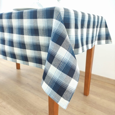 Toalha de mesa xadrez azul, branco e cinza sobre mesa de madeira.