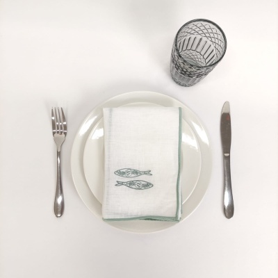 Conjunto de mesa com prato branco, guardanapo com bordado de peixes, talheres e copo padrão geométrico