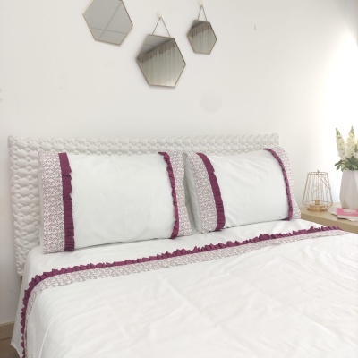 Conjunto de cama branco com detalhes em roxo e cabeceira estofada numa decoração de quarto moderna.