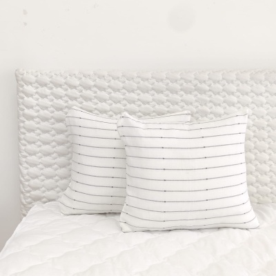 Duas almofadas brancas com riscas horizontais sobre cabeceira branca acolchoada e edredão branco
