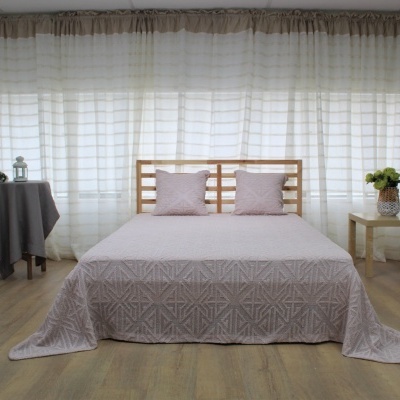 Quarto com cama de madeira clara, colcha e almofadas rosa, mesas laterais com decoração e cortinas brancas