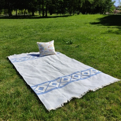 Tapete branco com padrão azul e almofada floral sobre relva verde