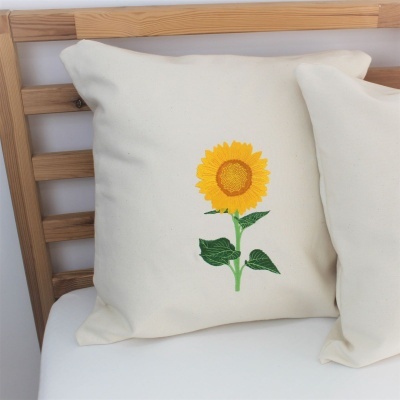 Almofada branca com bordado de girassol amarelo e verde sobre cama de madeira