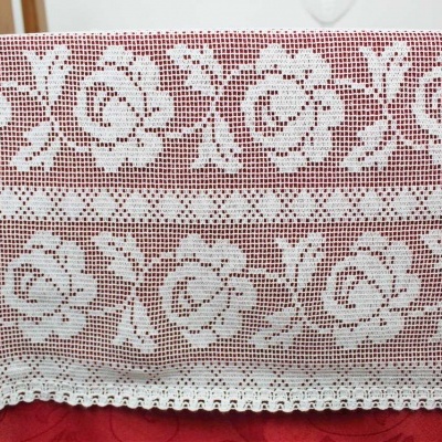 Cobertura de mesa em croché branco com padrão floral sobre mesa com toalha vermelha