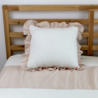 Almofada branca com franja rosa sobre cama com roupa de cama branca e rosa