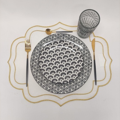 Conjunto de pratos e talheres com copo sobre jogo americano branco e dourado