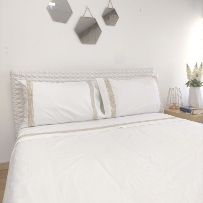 Cama com roupa de cama branca e cabeceira trançada, com mesa de cabeceira e decoração simples e moderna.