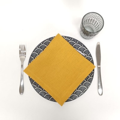 Prato decorativo com guardanapo amarelo, talheres metálicos e copo de vidro num conjunto de mesa