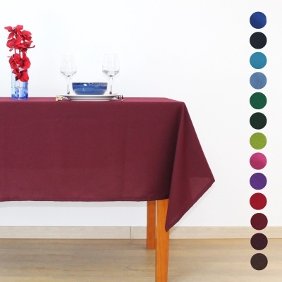 Toalha de mesa bordô sobre mesa de madeira com copos, prato e jarro com flores vermelhas