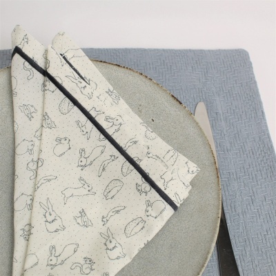 Guardanapo com padrão de coelhos e cenouras sobre prato cinza e base azul claro