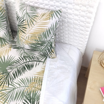 Conjunto de roupa de cama com estampado de folhas tropicais em cama com cabeceira branca e mesa de cabeceira