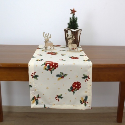 Caminho de mesa de Natal branco com padrão de bolas vermelhas e azevinho verde, com mini árvore e figuras de rena numa mesa de madeira.