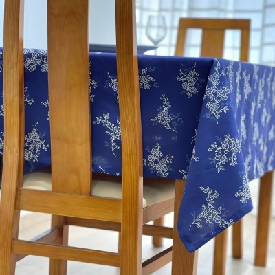 Toalha de mesa azul com padrão branco floral sobre mesa e cadeiras de madeira em ambiente claro