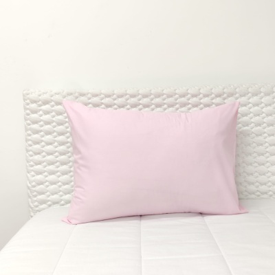 Travesseiro rosa com fronha lisa sobre cama branca com encosto acolchoado