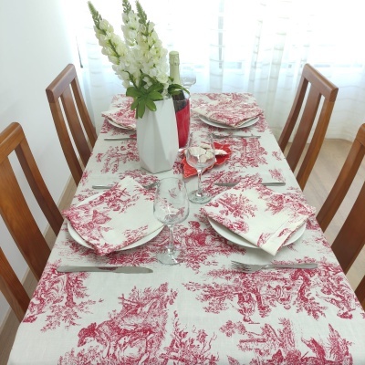 Mesa de jantar posta com toalha e guardanapos vermelhos e brancos, vasos com flores e garrafa de vinho