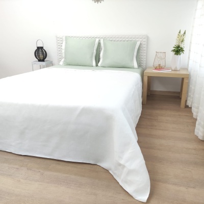 Cama de casal com roupa de cama branca e almofadas verdes