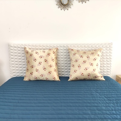 Cama com edredão azul e duas almofadas bege com padrão floral, encosto branco texturizado