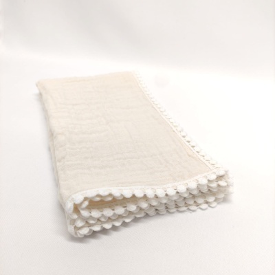 Toalha ou pano claro com pompons brancos nas bordas