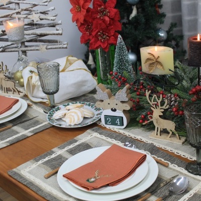 Mesa de jantar decorada para Natal com pratos, copos, velas e enfeites natalícios