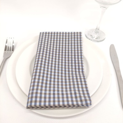 guardanapo xadrez azul claro, branco e castanho sobre pratos brancos com talheres e taça