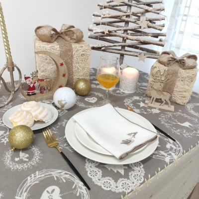 Mesa de Natal decorada com guardanapo, pratos, talheres, taça, velas, bolachas, enfeites dourados e presentes em papel rústico