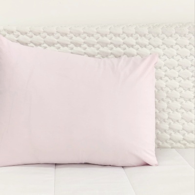 Travesseiro rosa claro sobre cama branca com cabeceira estofada branca