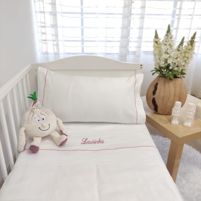 Cama de bebé com roupa branca bordada e peluche de alho sentado.