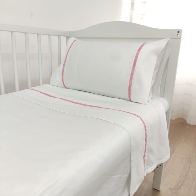 Cama branca com jogo de lençóis brancos e bordado rosa simples