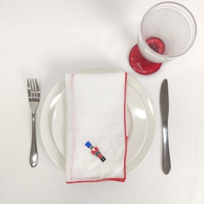 Conjunto de jantar com prato branco, guardanapo com borda vermelha e soldadinho de chumbo, talheres de metal e copo com base vermelha