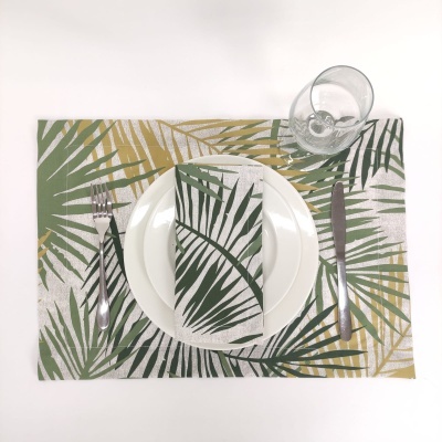 Mesa posta com conjunto individual e guardanapo estampados com folhas, prato branco, talheres de metal e copo de vidro