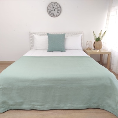 Cama de casal com roupa de cama branca e verde água, relógio de parede, mesa com vaso decorativo e flores