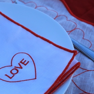 Guardanapos de tecido branco bordados com a palavra 'LOVE' e padrão de corações vermelhos