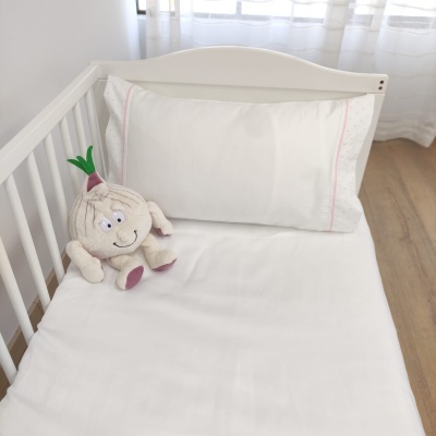 Berço branco com roupa de cama branca e peluche de alho sentado